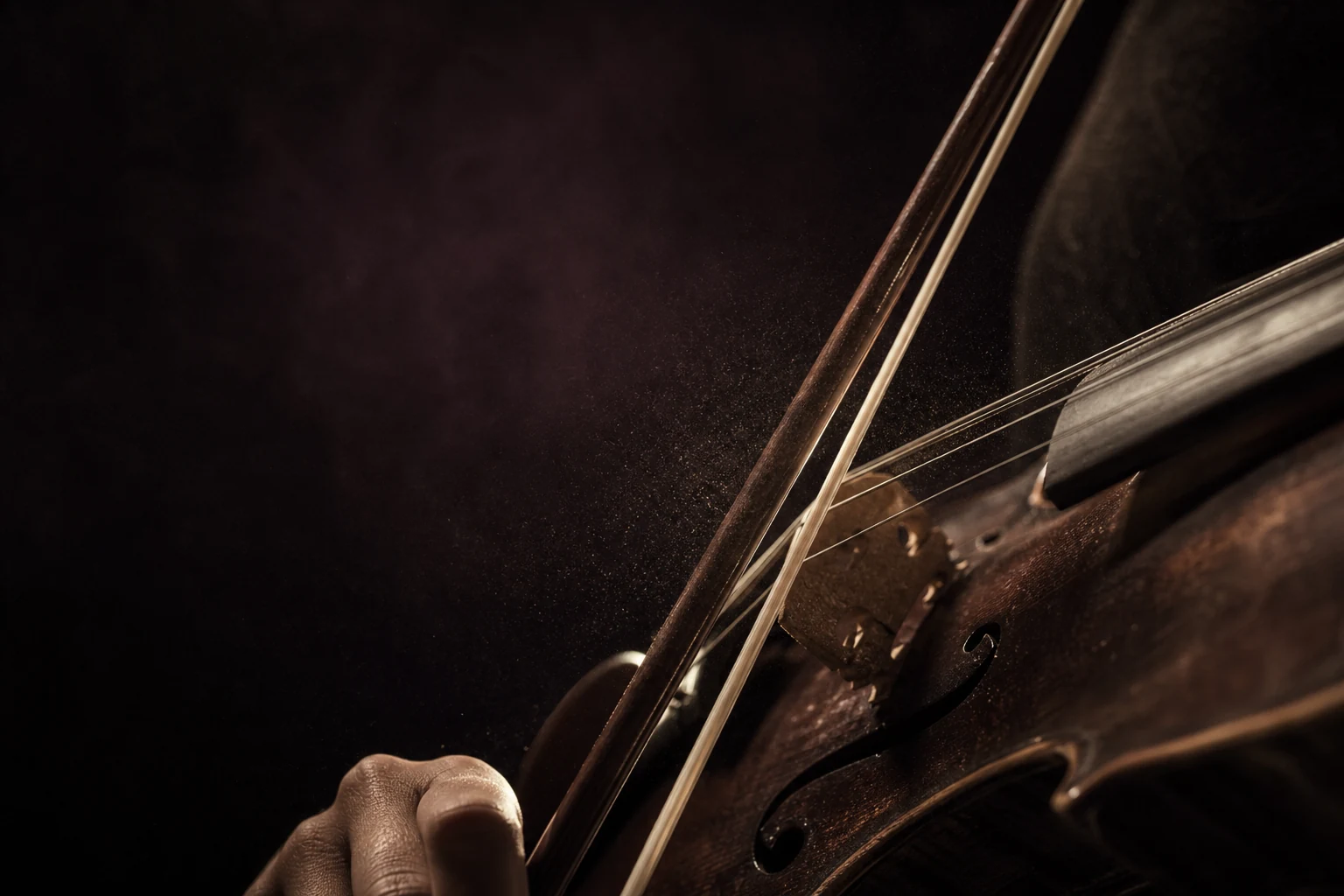 A violin bow meeting the strings in warm, low light